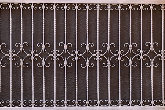 Wrought iron security grille provides a protective barrier with an elegant, traditional design featuring decorative twisted vertical bars and ornate scrollwork patterns