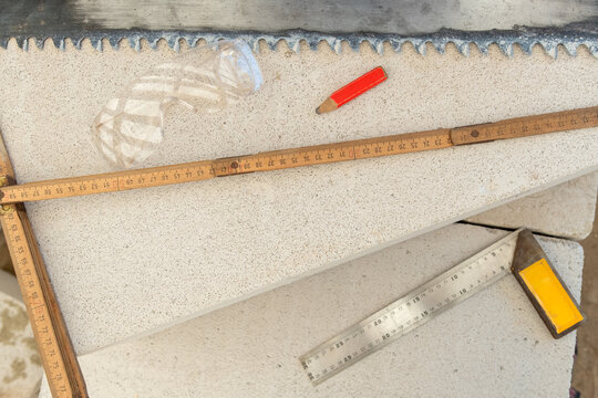 Folding ruler, try square, pencil and safety glasses arranged in a flat lay on textured concrete, evoking construction planning, woodworking precision and DIY craftsmanship