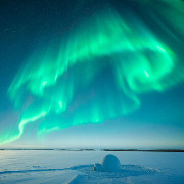 Cozy igloo glowing in a snowy field on a clear winter night, beneath the colorful northern lights. Aurora borealis and polar lights. Christmas postcard