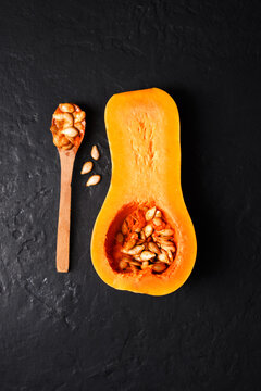 Butternut squash half with seeds and wooden spoon on black stone background. Minimal autumn food composition with pumpkin and seasonal ingredients