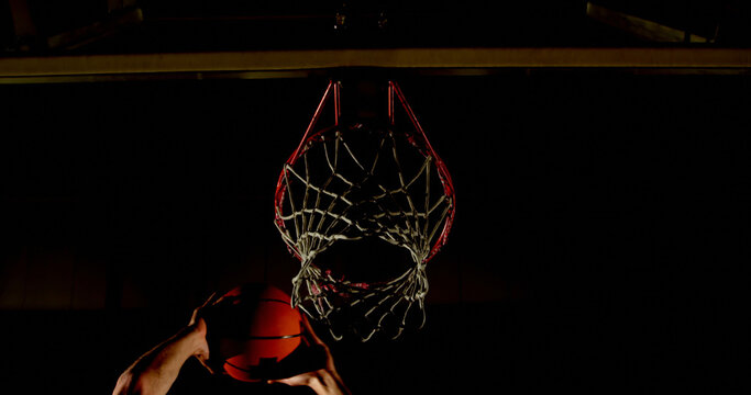A basketball player scores a basket in a dimly lit gym