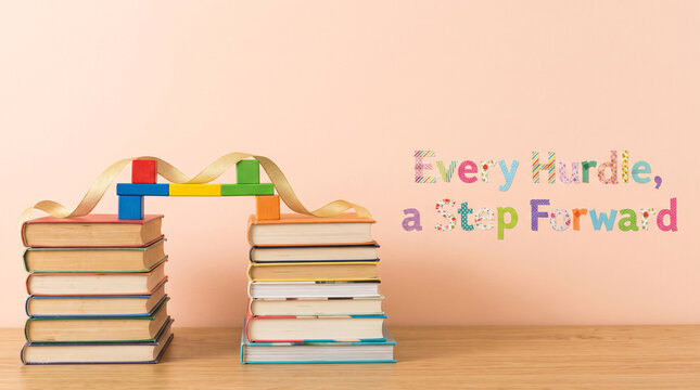 Two stacks of hardcover books connected by a colorful toy bridge with an inspirational text on a wall with background decorative letters against light background miniature wooden bridge