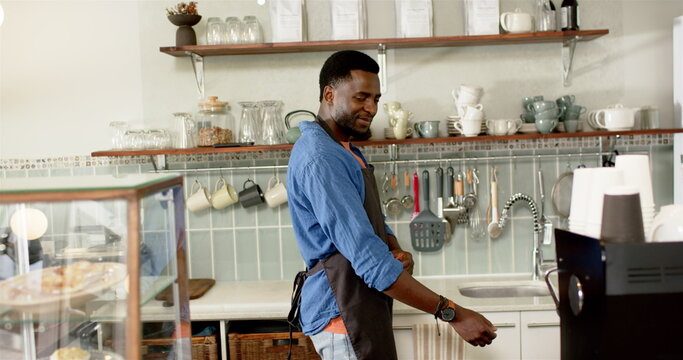 Young African American male barista in a cafe, tying an apron around his waist