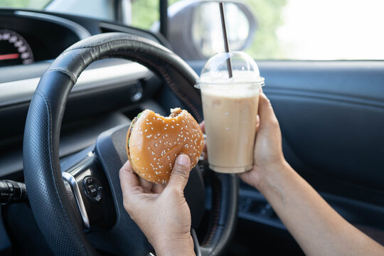 Asian woman driver hold ice coffee cup and sandwich bread for eat and drink in car, dangerous and risk an accident.
