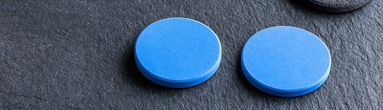 Two Blue Discs on Dark Surface: Two bright blue, round objects are positioned on a dark, textured surface, suggesting a clean and minimalist design.