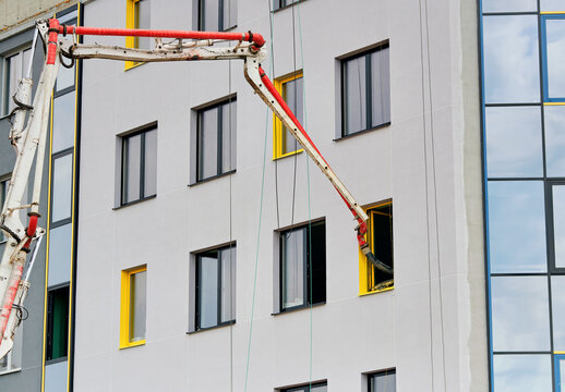 Concrete pump boom arm inserting its delivery hose into window of multi story building under construction. Concrete placement boom arm extending to deliver concrete inside residential building facade