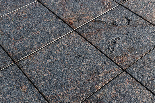 Textured dark stone tiles arranged in a diagonal geometric pattern with weathered surfaces and subtle brown highlights, close up architectural flooring detail