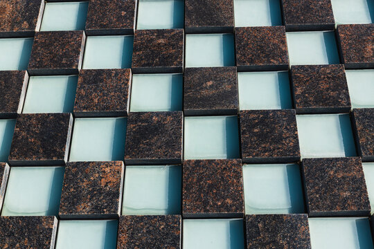 Abstract geometric arrangement of dark textured squares and pale glass panels forming a modern repeating architectural surface pattern in close up
