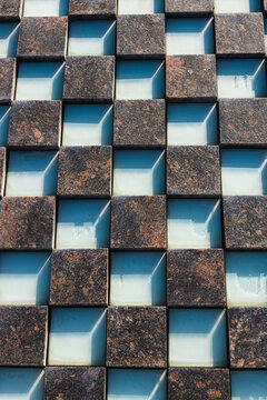 Abstract geometric facade with alternating dark textured panels and recessed blue glass sections in a repeating architectural grid pattern