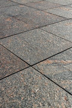 Close up of weathered gray stone pavement with intersecting dark grout lines and mottled reddish texture forming an abstract geometric surface pattern
