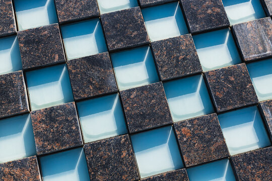 Repeating geometric arrangement of dark textured square tiles and recessed pale blue compartments in an abstract architectural surface pattern