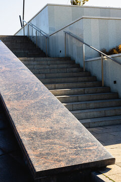 Concrete stairway with metal railings and broad sloped ramp beside a modern building in bright daylight, showing geometric outdoor architectural details