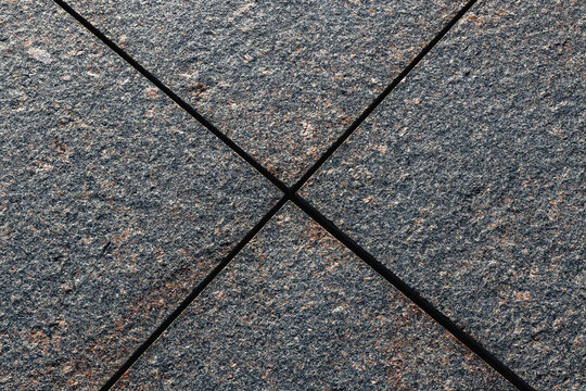 Black crossed lines over a mottled gray textured surface with centered geometric intersection, abstract overhead composition and neutral background pattern