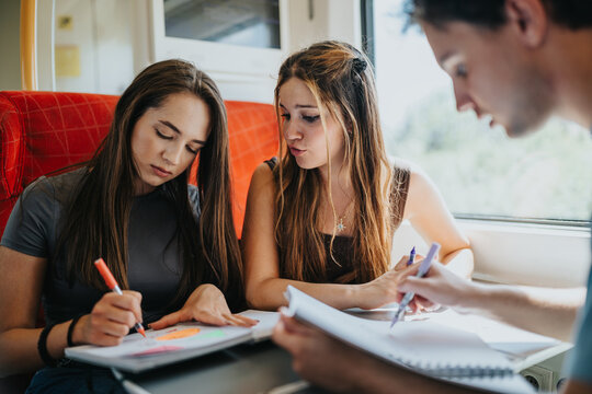 Students study, write notes and draw together on a train during their daily commute, supporting education and learning on the go.