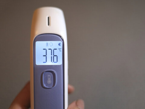 Digital thermometer showing 37.6 degrees Celsius in a hand, with a lit display for checking body temperature during personal health monitoring and fever screening, beside open copy space on the right.