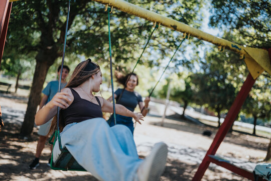 Friends swing together at a sunny park playground, enjoying playful outdoor leisure, friendship and student life.