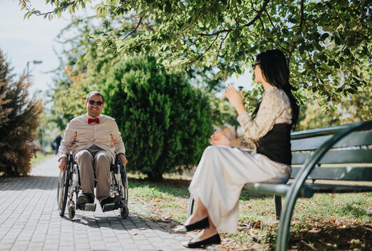Man in a wheelchair talks with his caregiver during an accessible outdoor park visit, representing disability support, mobility and inclusive everyday life.