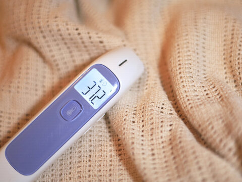 Digital thermometer displaying 37.2 on a knitted blanket shows a body temperature reading on its screen, a handheld medical device for fever checks and routine health monitoring in home healthcare.