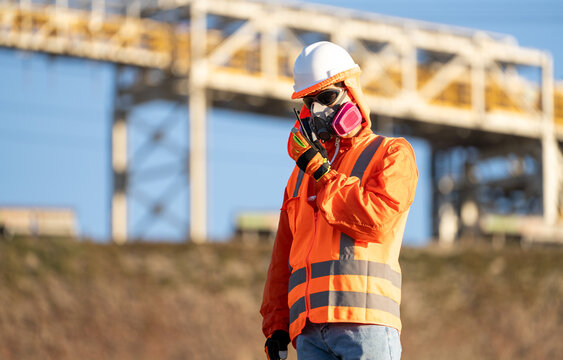 Mining worker wearing a respirator and using a two-way radio near an industrial plant in northern Chile
