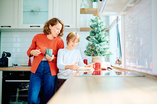 Mother and son sharing a festive moment, preparing food together beside a Christmas tree in their bright home kitchen