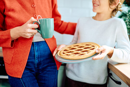 Woman and child sharing a lattice pie and warm drink in a bright kitchen during a festive holiday gathering at home
