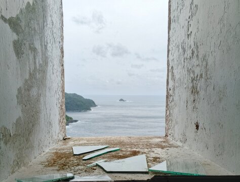 Panoramic tropical ocean view framed through old broken glass window ledge of abandoned building