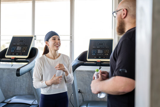 Woman and man talk beside treadmills in a bright gym