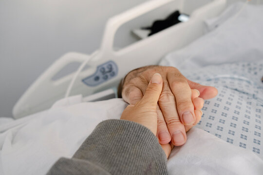 Close-up of supportive hand holding hospital patient in bed