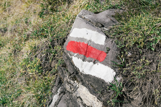 Mountain hiking trail marker on rock. Three stripes icon for alpine hiking in Switzerland. White, red and white painted lines to guide hikers on trails. Selective focus.