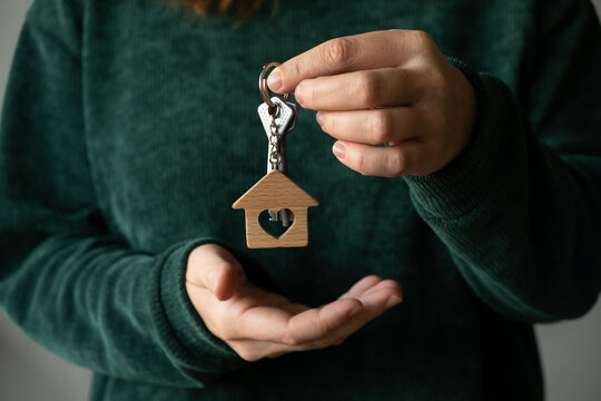 Woman shows keys to her new house standing in front of gray wall. Buying or renting real estate. 