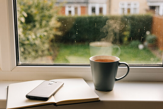 Tea and a face down phone beside a notebook on a windowsill