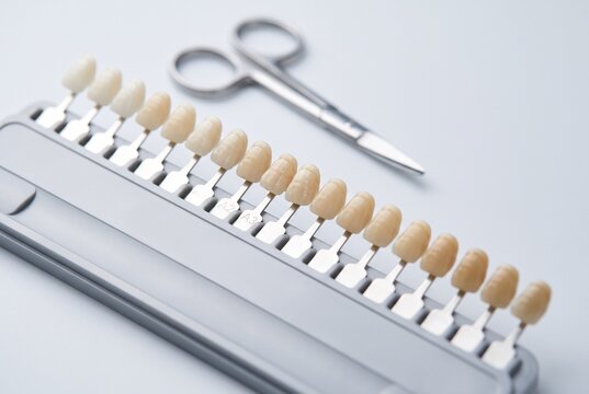 Dental shade guide with gradient tooth color samples and surgical scissors on light gray background