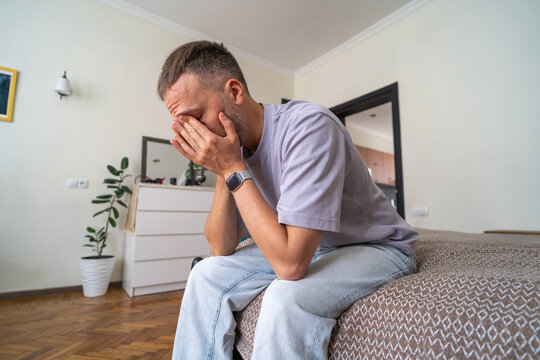 Grief and Loss, Devastated Man Sitting on Bed Covering Face in Sadness and Emotional Pain.