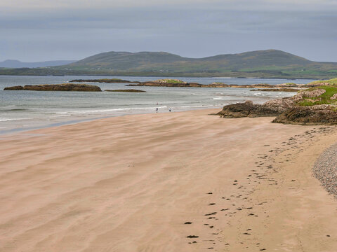 Wide sandy beach meets ocean with rocky outcrops and rolling hills in background