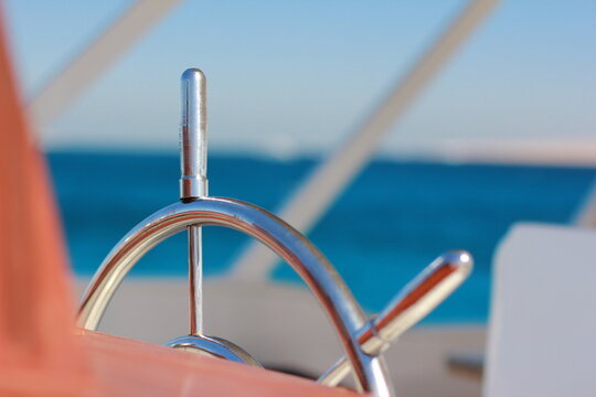 Stainless steel helm control wheel of cruise yacht over bright turquoise sea ripples closeup