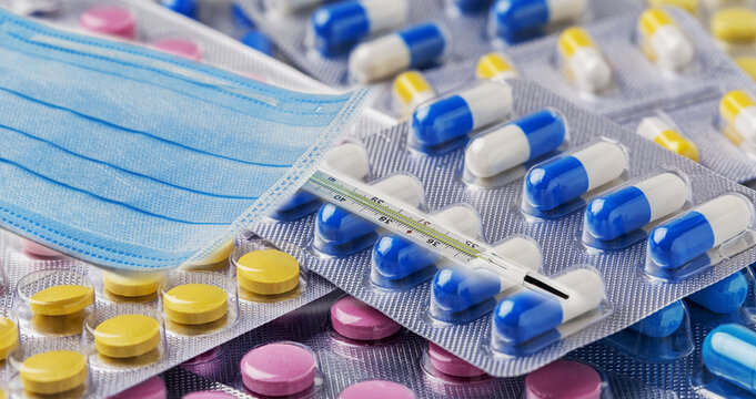 medical protective mask and thermometer against a background of medications