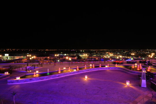 Panoramic landscape of dark night city panorama with colorful neon light fountain installation on hotel territory in Egypt