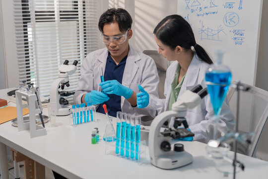 Asian male and female scientists collaborating on research with micropipette and clipboard in laboratory