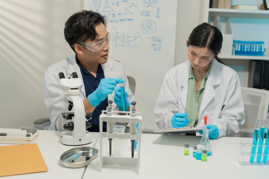 Asian male and female scientists collaborating on research with micropipette and clipboard in laboratory