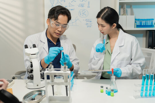 Asian male and female scientists collaborating on research with micropipette and clipboard in laboratory