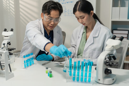 Asian male and female scientists collaborating on research with micropipette and clipboard in laboratory