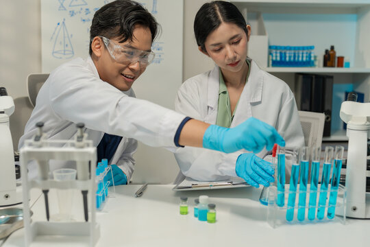 Asian male and female scientists collaborating on research with micropipette and clipboard in laboratory