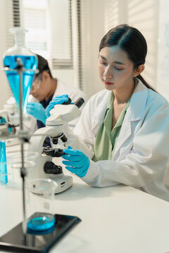 Asian male and female scientists collaborating on research with micropipette and clipboard in laboratory