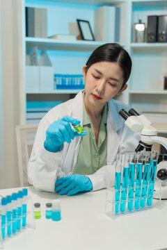 Asian female scientist using dropper with flask and microscope in chemical laboratory