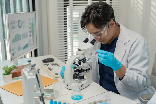 Asian male scientist using micropipette for chemical experiment with microscope in laboratory
