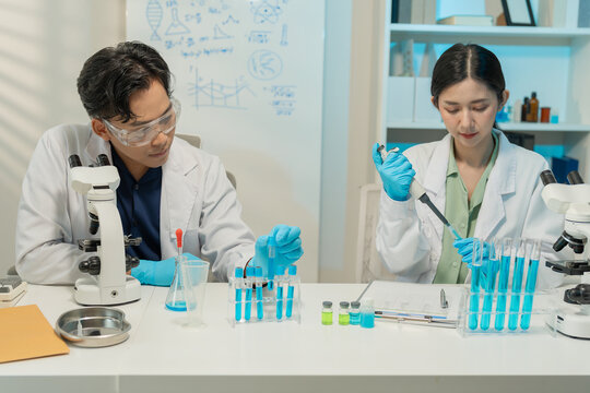 Asian male and female scientists collaborating on research with micropipette and clipboard in laboratory