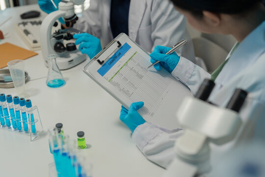 Asian male and female scientists collaborating on research with micropipette and clipboard in laboratory
