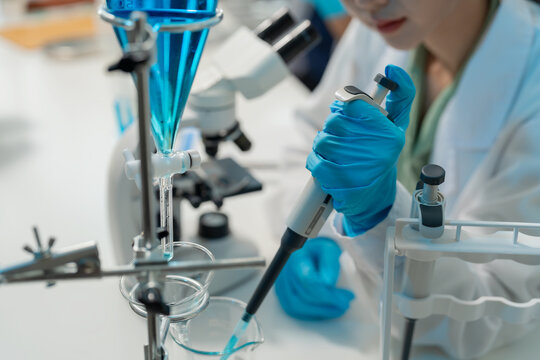 Asian female scientist using dropper with flask and microscope in chemical laboratory