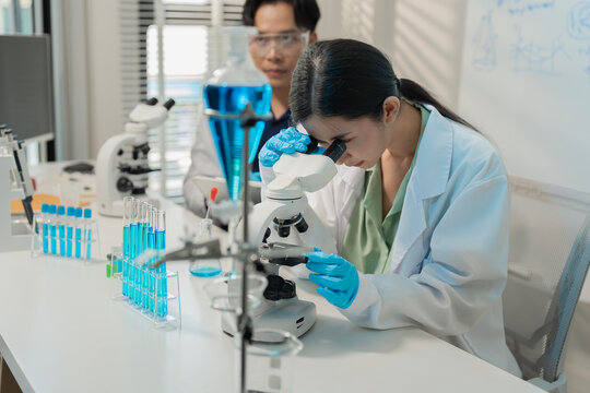 Asian male and female scientists collaborating on research with micropipette and clipboard in laboratory