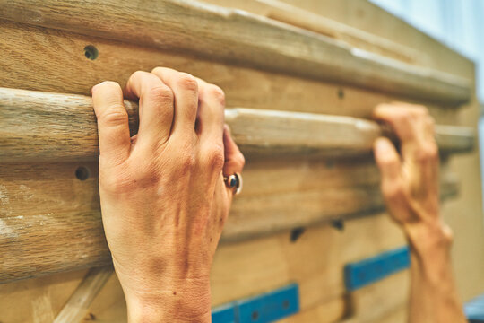 Both Hands Gripping a Wooden Campus Board at a Climbing Gym